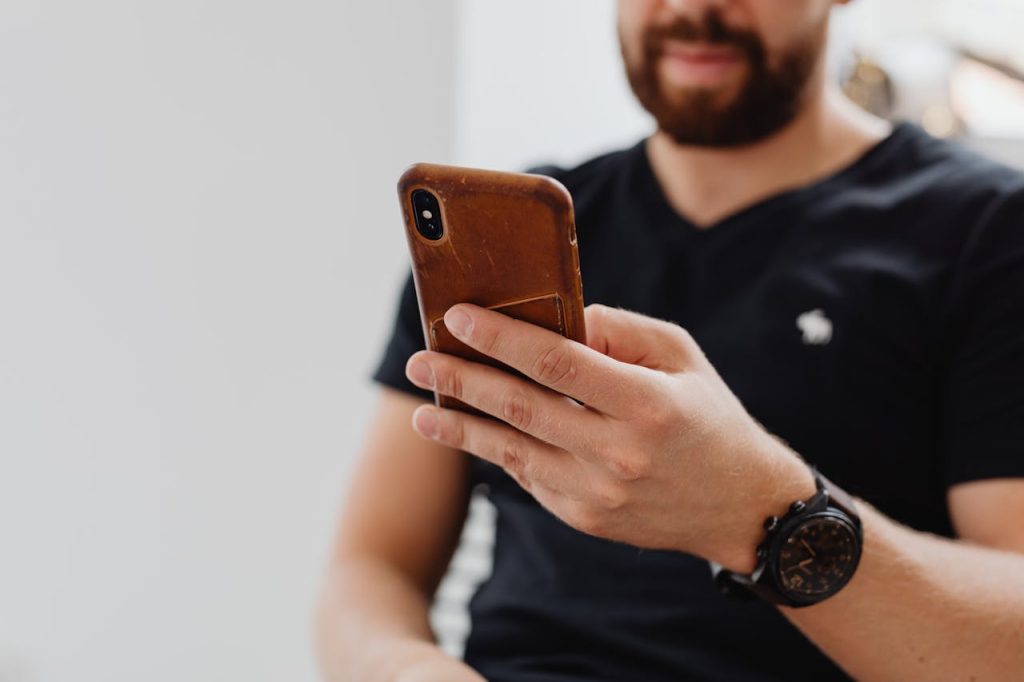 A bearded man using a smartphone indoors, casually dressed.